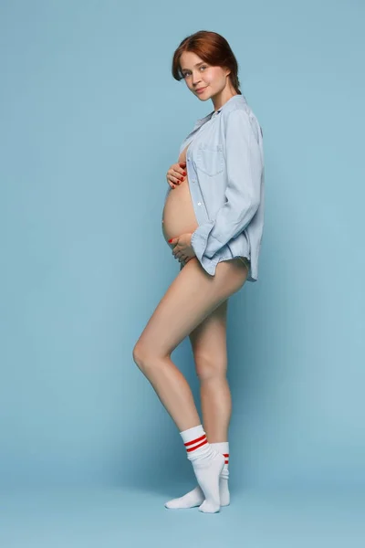 Młoda piękna kobieta w ciąży, stojąc na niebieskim tle — Zdjęcie stockowe