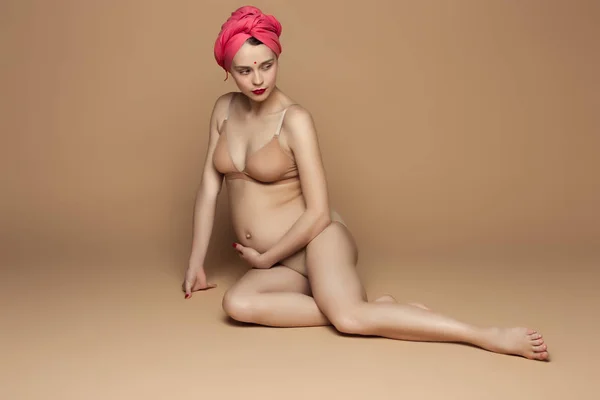 Joven hermosa mujer embarazada sentada sobre fondo marrón —  Fotos de Stock