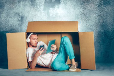 Introvert concept. Man sitting inside box and working with phone clipart