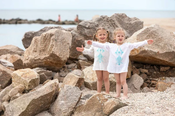 Dzieci na brzegu morza. Bliźnięta stojący przed kamieniami i wody morskiej. — Zdjęcie stockowe