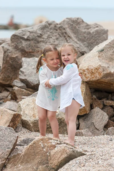 Children on the sea beach. Twins standing against stones and sea water. — Stock Photo, Image