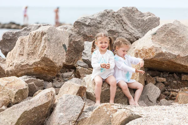 Dzieci na brzegu morza. Twins, siedząc przed kamieniami i wody morskiej. — Zdjęcie stockowe