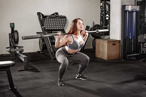 Attractive fit woman works out with dumbbells as a fitness conceptual over gray gym background.