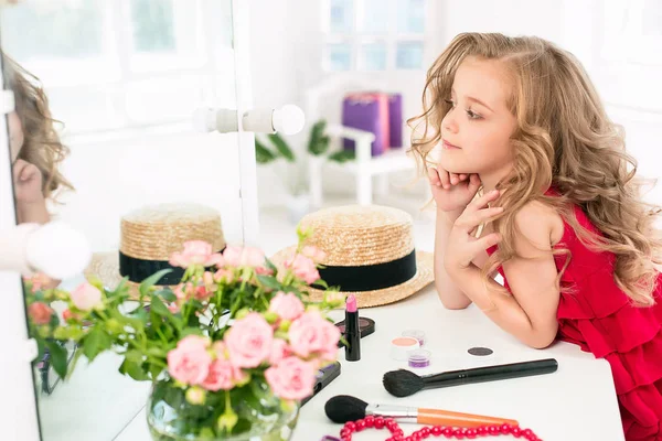 Ein kleines Mädchen mit Kosmetik. sie sitzt im Schlafzimmer der Mutter neben dem Spiegel. — Stockfoto