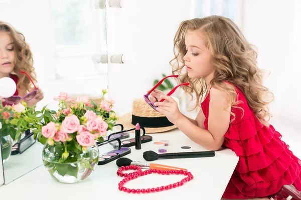 Ein kleines Mädchen mit Kosmetik. sie sitzt im Schlafzimmer der Mutter neben dem Spiegel. — Stockfoto