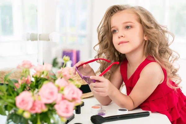 Ein kleines Mädchen mit Kosmetik. sie sitzt im Schlafzimmer der Mutter neben dem Spiegel. — Stockfoto