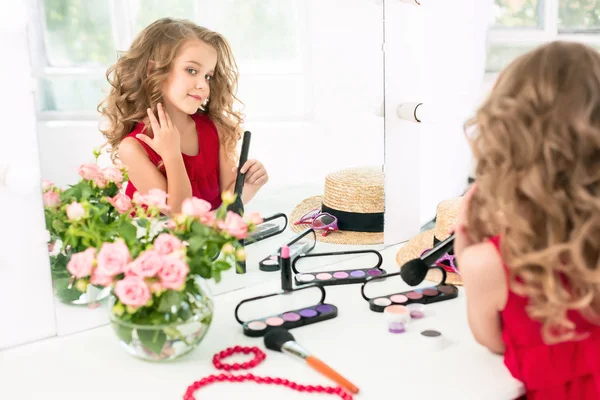 Маленькая девочка с косметикой. Она в спальне матери, сидит у зеркала . — стоковое фото