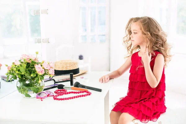 Ein kleines Mädchen mit Kosmetik. sie sitzt im Schlafzimmer der Mutter neben dem Spiegel. — Stockfoto