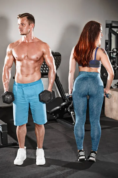 sport fit couple at gym. work in pairs with dumbbells