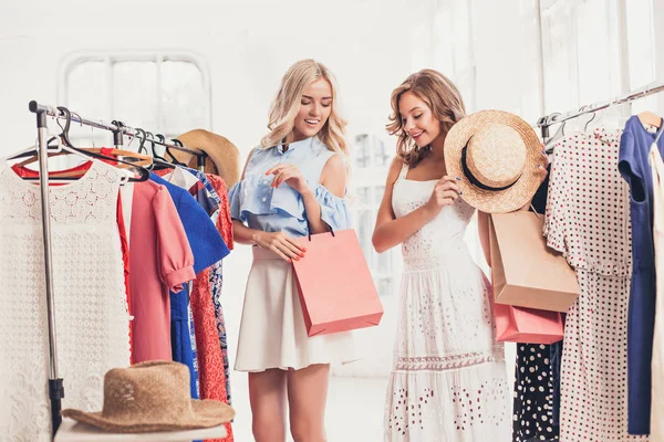 Las dos chicas guapas jóvenes mirando vestidos y probarlo al elegir en la tienda — Foto de Stock