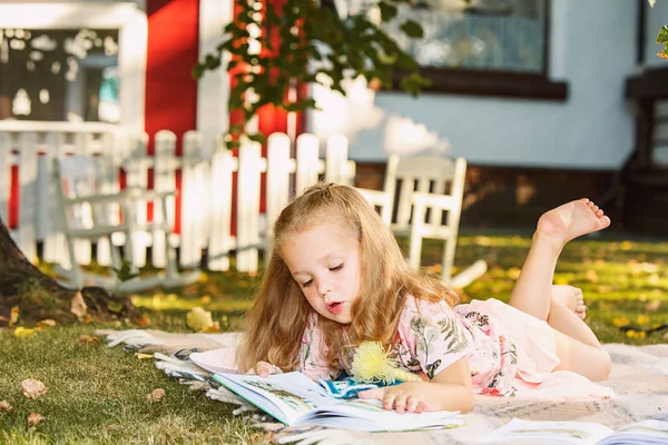 Linda niña rubia leyendo libro fuera de la hierba —  Fotos de Stock