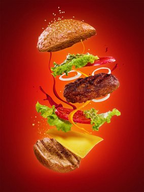 Kırmızı zemin üzerinde uçan malzemeler olan hamburger.