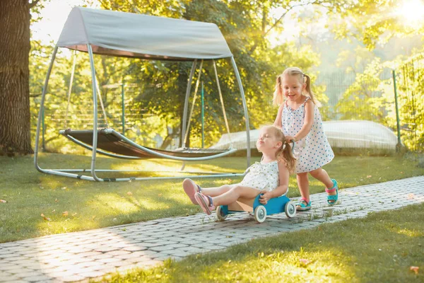 Meninas loiras bonitos montando um carro de brinquedo no verão . — Fotografia de Stock