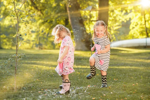 As meninas loiras bonitos em botas de borracha brincando com salpicos de água no campo no verão — Fotografia de Stock