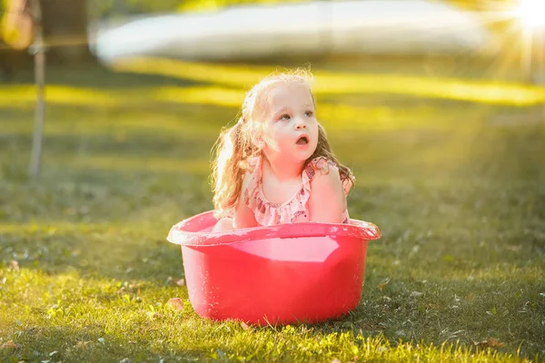 La linda niña rubia jugando con salpicaduras de agua en el campo en verano — Foto de Stock