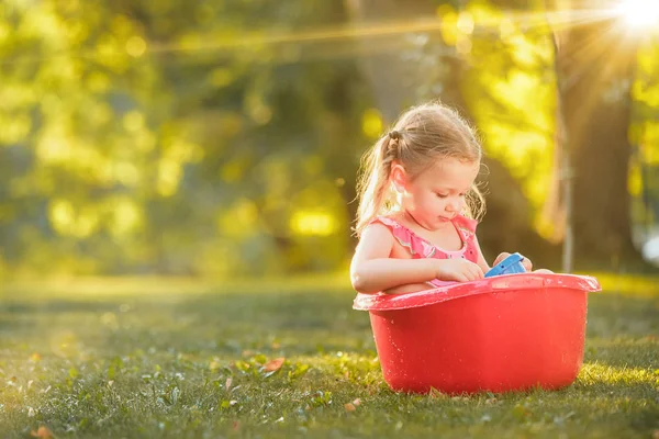 Cute dziewczynka blond, grając z wody plamy na polu w lecie — Zdjęcie stockowe