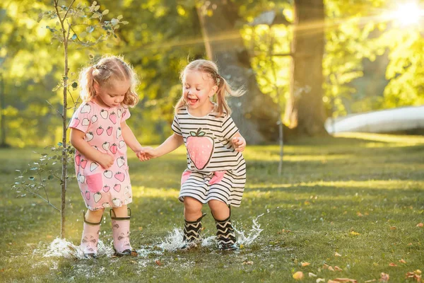 Ładny blond dziewczynki w gumowe buty, gra z wodą rozpryskową na polu w lecie — Zdjęcie stockowe