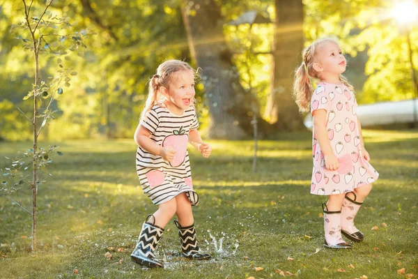 Симпатичные девчонки в резиновых сапогах, играющие с водяными баллончиками на поле летом — стоковое фото