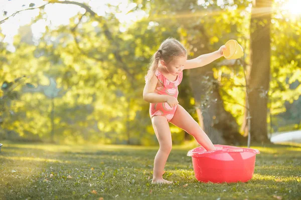 Cute dziewczynka blond, grając z wody plamy na polu w lecie — Zdjęcie stockowe