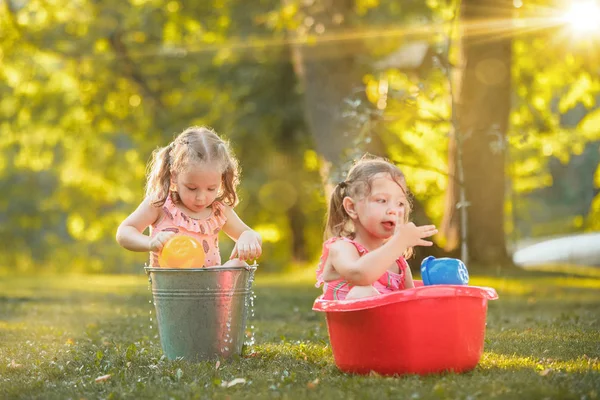 Las niñas rubias lindas jugando con salpicaduras de agua en el campo en verano — Foto de Stock