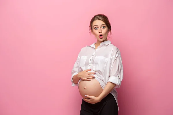 Fiatal gyönyörű terhes nő áll rózsaszín háttér — Stock Fotó