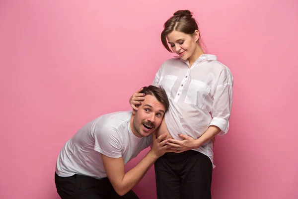 Handsome man is listening to his beautiful pregnant wifes tummy and smiling — Stock Photo, Image