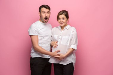 Yakışıklı adam güzel hamile karısının karnını dinliyor ve gülümsüyor.