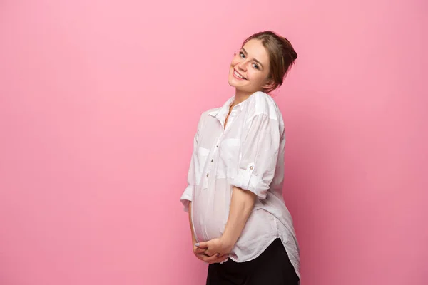 Joven mujer embarazada hermosa de pie sobre fondo rosa — Foto de Stock