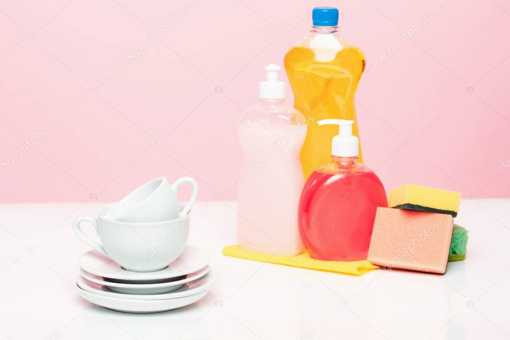 Several plates, a kitchen sponges and a plastic bottles with natural dishwashing liquid soap in use for hand dishwashing.