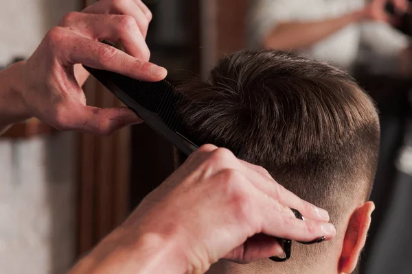 Las manos de peluquero haciendo corte de pelo a un joven en la barbería —  Fotos de Stock
