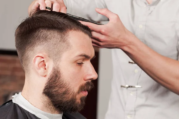 Las manos de peluquero haciendo corte de pelo a un joven en la barbería — Foto de Stock