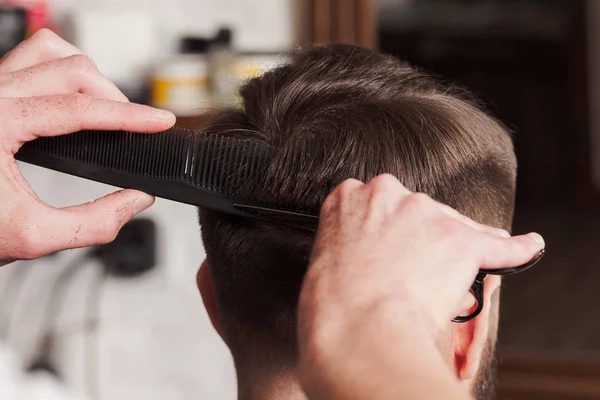 Die Hände des Friseurs, der einem jungen Mann im Friseursalon die Haare schneidet — Stockfoto