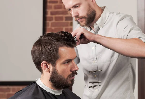 Giovane bel barbiere che fa taglio di capelli di uomo attraente in barbiere — Foto Stock