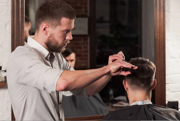 Молодий красивий перукар робить стрижку привабливої людини в перукарні — стокове фото