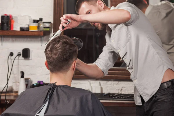 Young handsome barber making haircut of attractive man in barbershop — Stock Photo, Image