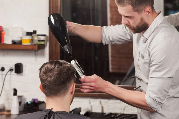 Joven peluquero guapo haciendo corte de pelo de hombre atractivo en la barbería — Foto de Stock