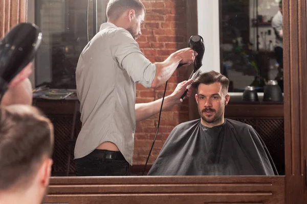 Young handsome barber making haircut of attractive man in barbershop — Stock Photo, Image