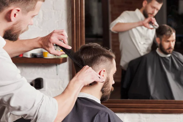 Jovem barbeiro bonito fazendo corte de cabelo de homem atraente na barbearia — Fotografia de Stock