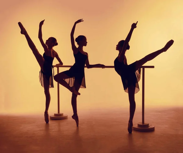 Композиція з силуетів трьох молодих танцюристів в балеті позує на помаранчевому тлі . — стокове фото