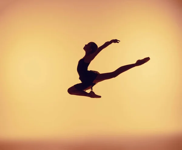 Belle jeune danseuse de ballet sautant sur un fond orange . — Photo