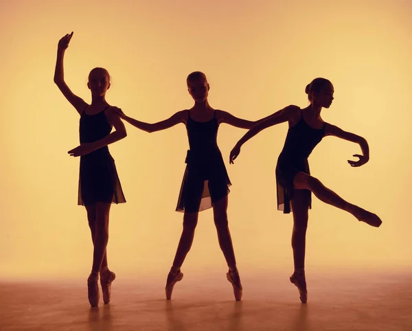 Composition à partir de silhouettes de trois jeunes danseurs en posture de ballet sur fond orange . — Photo