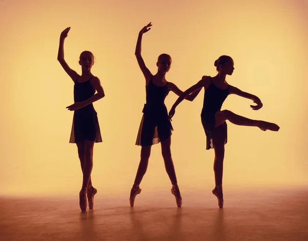 Komposition aus Silhouetten dreier junger Tänzer in Ballettpositionen auf orangefarbenem Hintergrund. — Stockfoto