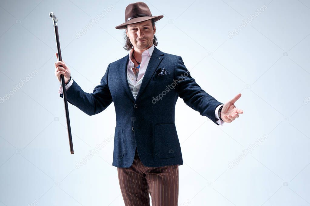 The mature man in a suit and hat holding cane.