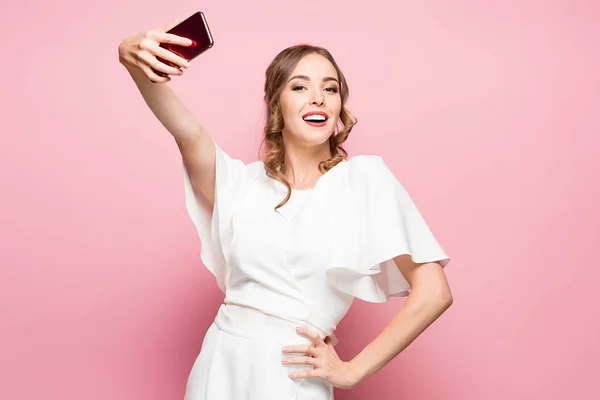 Retrato de uma jovem mulher atraente fazendo foto selfie com smartphone em um fundo rosa — Fotografia de Stock