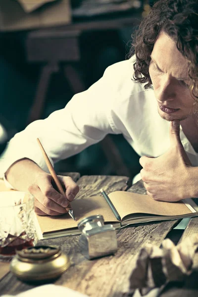 Yazar iş başında. Masada oturan ve bir şey onun eskiz defteri yazma yakışıklı genç yazar