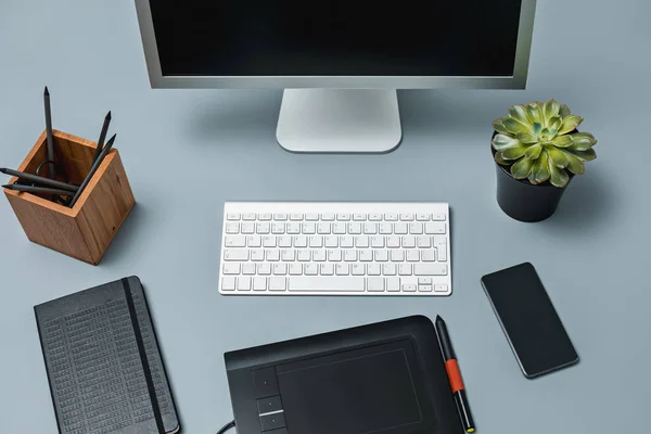 A mesa cinza com laptop, bloco de notas com folha em branco, vaso de flor, estilete e tablet para retoque — Fotografia de Stock