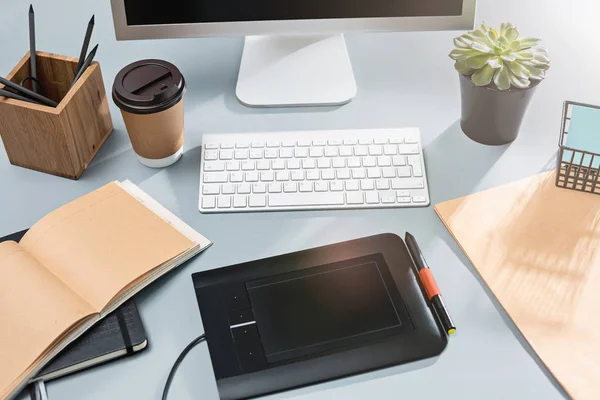 A mesa cinza com laptop, bloco de notas com folha em branco, vaso de flor, estilete e tablet para retoque — Fotografia de Stock