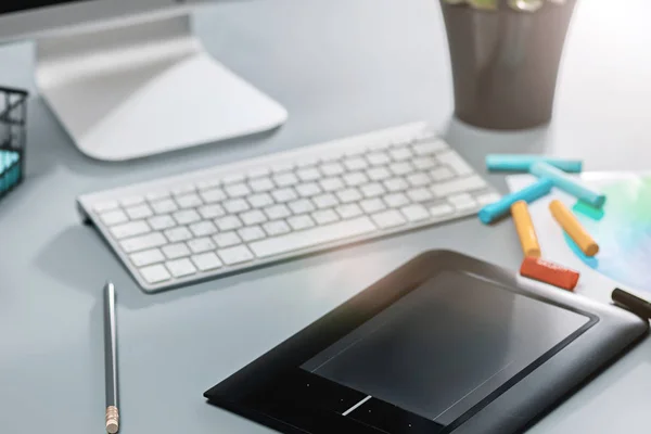 A mesa cinza com laptop, bloco de notas com folha em branco, vaso de flor, estilete e tablet para retoque — Fotografia de Stock