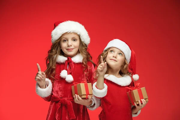 Duas meninas felizes em chapéus de Papai Noel com caixas de presente no estúdio — Fotografia de Stock