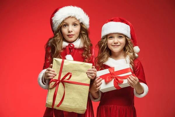 Duas meninas felizes em chapéus de Papai Noel com caixas de presente no estúdio — Fotografia de Stock